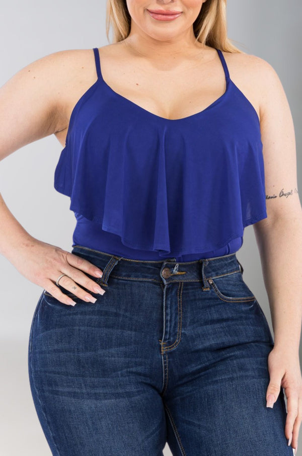 A plus-size model wearing a blue, thin-strapped, sleeveless bodysuit with ruffle detail, paired with jeans.